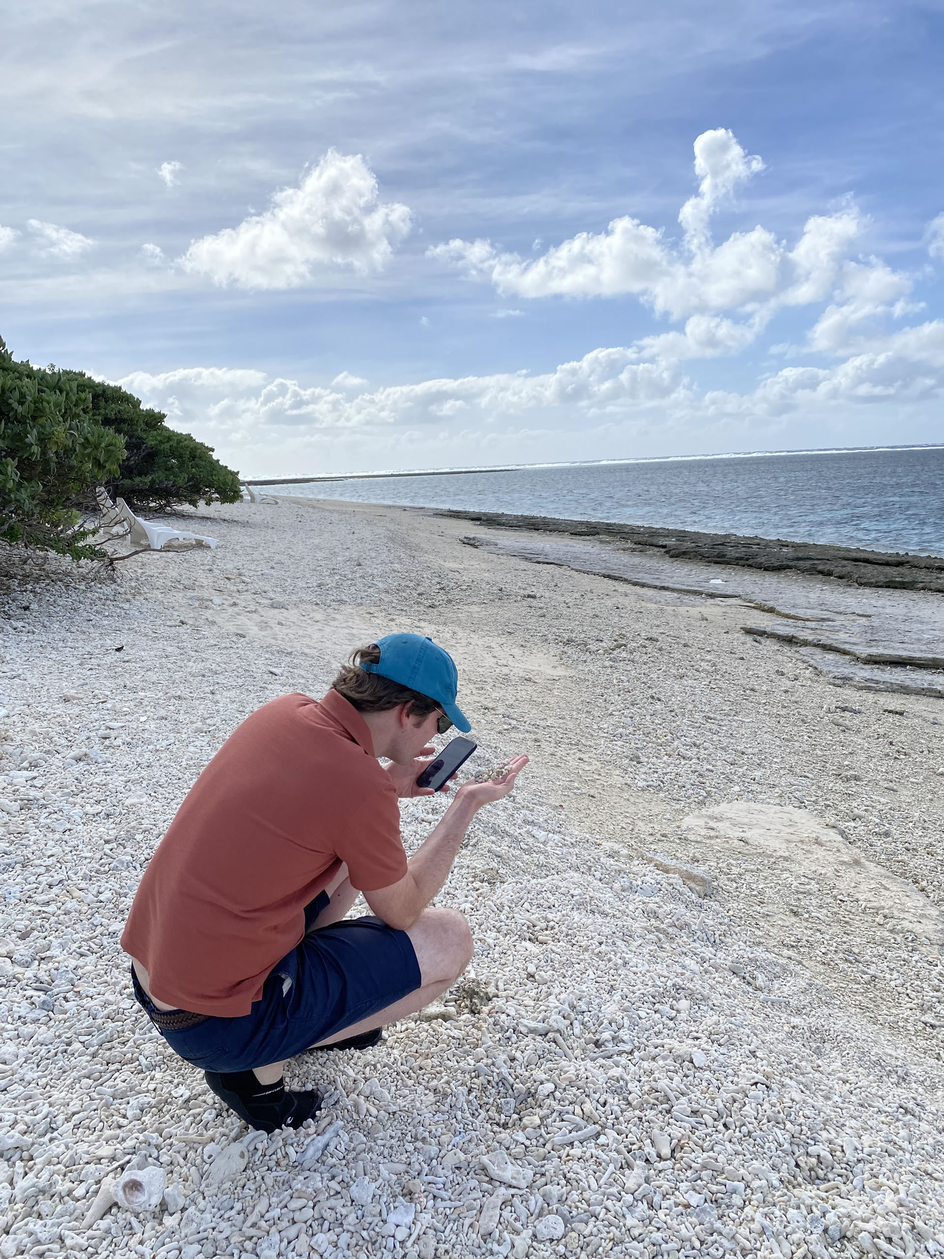 David M. Green takes a photo of a handful of coral washed up on the beach at Lady Elliot Island, 10 May 2025